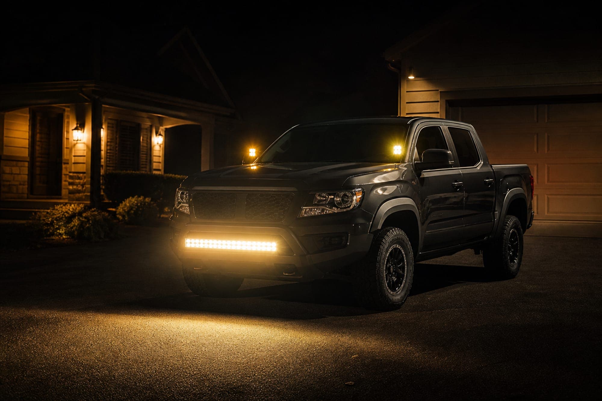 Dark pickup truck with a front LED light bar illuminated in a driveway at night